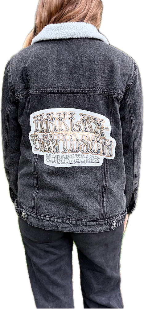 Person wearing a black denim jacket with a graphic design on the back