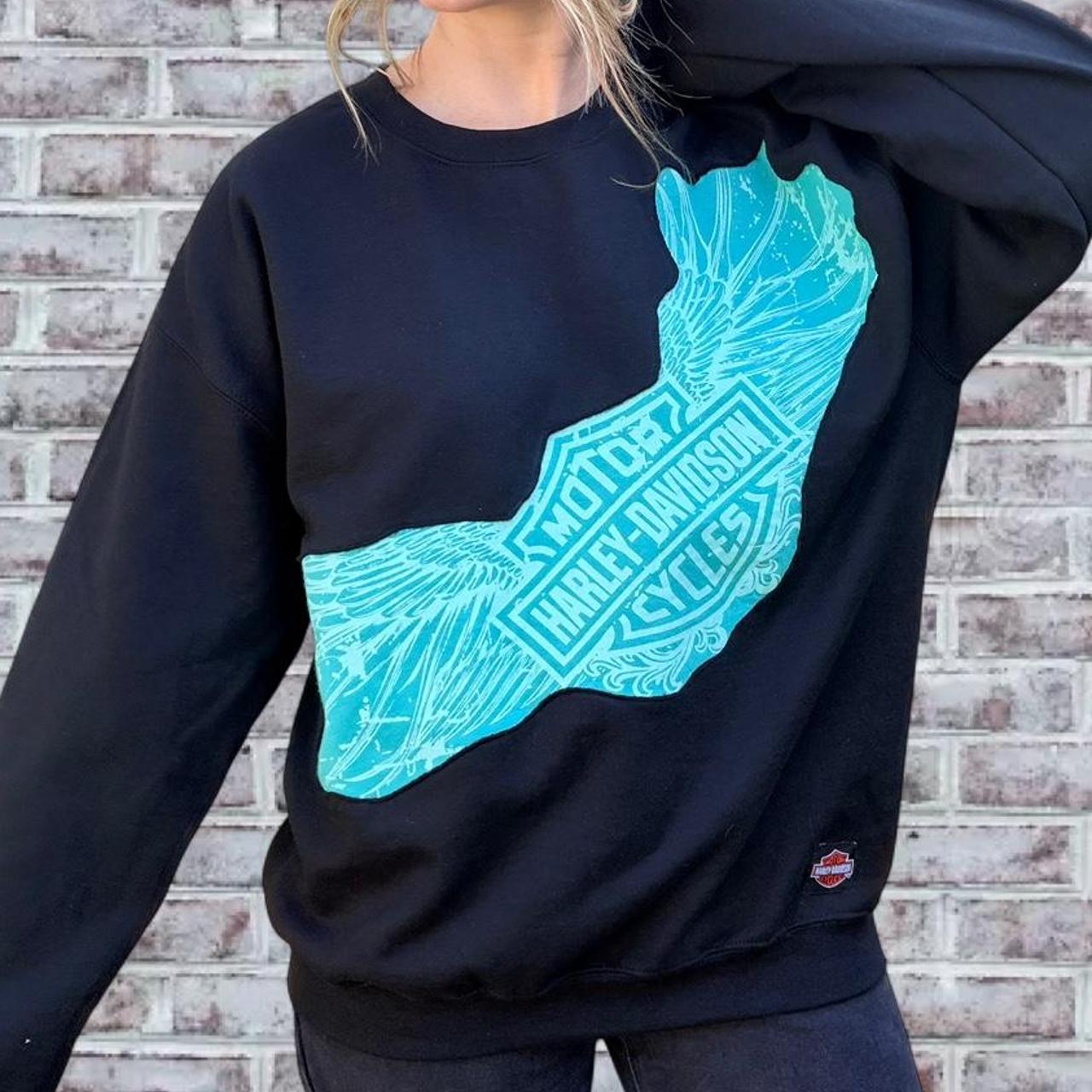 Black sweatshirt with a blue graphic design against a brick wall